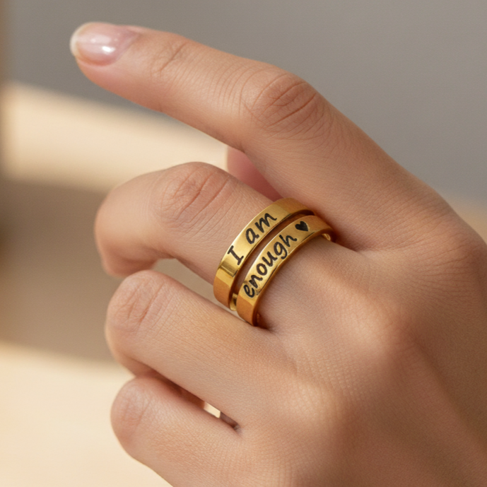 Gold ring with engraved text on a hand against a neutral background